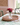 Vase with pink flowers on a woven tray on a table with a green and white patterned tablecloth.