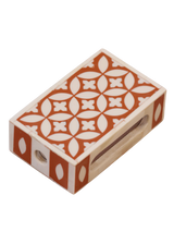 A handmade matchbox holder with a geometric pattern in orange and white colors, equipped with a slot to hold matches.